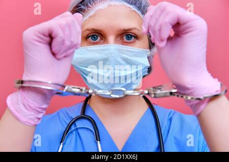 Eine Krankenschwester auf rosa Hintergrund zeigt Hände in Handschellen, Nahaufnahme. Arzt für eine Bestechung von einem Patienten verhaftet, Konzept Stockfoto