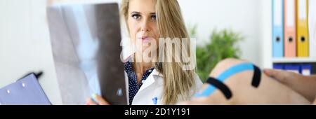 Ärztin mit untersucht eine Röntgenaufnahme des Beins neben dem Patienten sitzt. Stockfoto