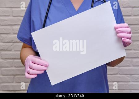 Doktor hält ein leeres leeres Blatt Papier, Kopierplatz für die Inschrift. Krankenschwester in blauer Uniform mit weißem Laken, Nahaufnahme Stockfoto