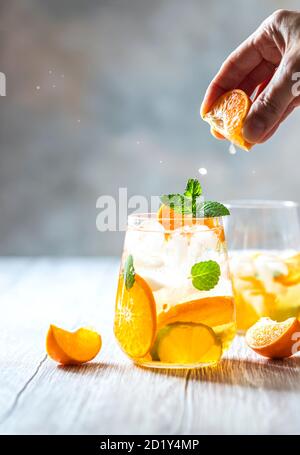 Hausgemachter erfrischender Eistee mit Orange und Zitrone auf einem rustikalen Holztisch. Sommerliches Erfrischungsgetränk-Konzept. Stockfoto