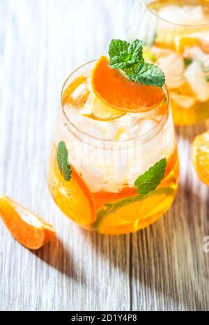 Hausgemachter erfrischender Eistee mit Orange und Zitrone auf einem rustikalen Holztisch. Sommerliches Erfrischungsgetränk-Konzept. Stockfoto