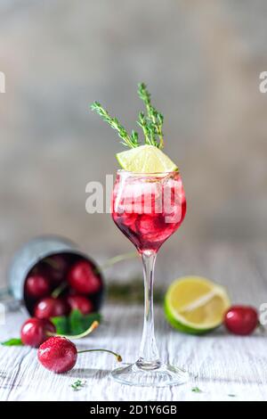 Kirschroter Cocktail mit Limette. Frischer Sommercocktail mit Kirschen, Thymian und Eiswürfeln. Stockfoto
