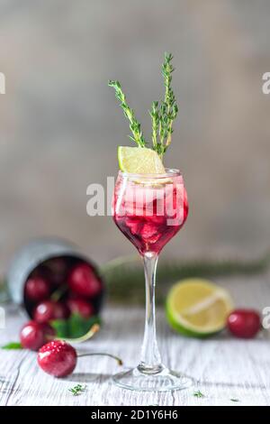 Kirschroter Cocktail mit Limette. Frischer Sommercocktail mit Kirschen, Thymian und Eiswürfeln. Stockfoto
