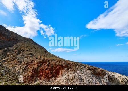 Schöne wilde rote Klippen, klarer blauer Himmel, Wolken. Diagonale Ansicht. Typisch griechische Landschaft. Akrotiri Halbinsel, Chania Region, Kreta Insel, Griechenland Stockfoto
