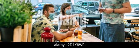 Pärchen mit Maske, die dem Kellner Essen bestellen Stockfoto