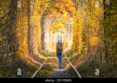 Junge Frau, die im Baumtunnel auf der Eisenbahn läuft Im Herbst Stockfoto