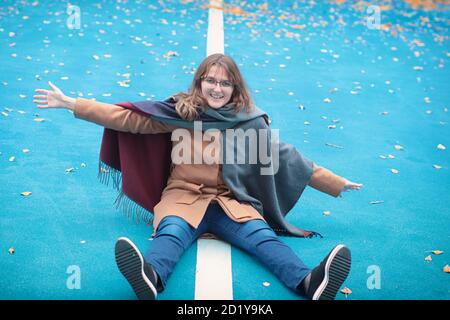 Fußballspielplatz im Freien auf der Straße. Eine junge Frau, die auf einem Hockeyplatz sitzt. Kaltes Wetter auf einem offenen Sportplatz mit blauer Oberfläche. Stockfoto