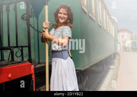 Eine junge Frau auf den Stufen des Autos Abfahrt Zug. Plattform im Rauch von einer Dampflokomotive. Mädchen in einem nebligen Dunst auf dem Hintergrund des tr Stockfoto