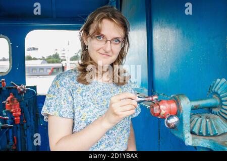 Spinnmechanismus in den Händen der Frauen. Das Mädchen in der Kabine einer Dampflokomotive. Vintage-Mechanismen im alten Zug. Weiblicher Portrait Lifestyle Stockfoto