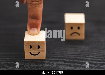 Hand wählen Smiley Gesicht und verschwommen traurig Gesicht Symbol auf Holz Würfel, Service-Bewertung, Zufriedenheit Konzept. Stockfoto