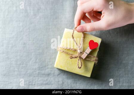 Natürliche handgemachte Seife mit Herz-Dekor auf einem Hintergrund aus Leinenstoff. Kinderhände halten Naturseife. Stockfoto