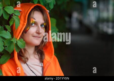 Ungewöhnlich gekleidete Frau mit einem leichten Wahnsinn in den Augen. Ein Mädchen in einem Fantasy-Helden-Kostüm und die Dunkelheit eines langen Korridors. Weibliche Porträt mit Stockfoto