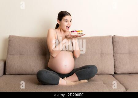 Glückliche hungrige Frau genießt es, köstliche Kuchen zu Hause zu entspannen essen. Leckere süße Lebensmittel während der Schwangerschaft Konzept. Stockfoto