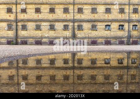 Alte verlassene Gefängnismauer und Zellfenster mit Metallstangen, Spiegelung der Gefängnismauer im Wasser auf dem Boden nach Regen Stockfoto