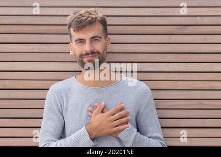 Gutmütiger gutaussehender Kerl hält Hände auf Herz, zeigt Liebe und Sympathie über Holzwand Hintergrund mit Kopierer Raum. Körpersprache und Liebe Feelin Stockfoto