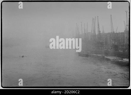 London Ansichten im Nebel November 1968 die Themse, London England bei nebligen Nebelverhältnissen. Blick nach Osten von der London Bridge mit Kräne und den Kais der Südseite der Themse Stockfoto