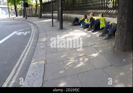 London, England, Großbritannien. Arbeiter, die während einer Pause auf dem Bürgersteig sitzen, bei der St. Pauls Kathedrale Stockfoto