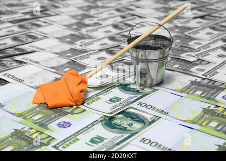 Geldwäsche. Das Konzept der Korruption. Ein Eimer Wasser und ein Mopp mit einem Lappen stehen auf den Dollar- und Euro-Scheinen. Sauber und schmutziges Geld. Stockfoto