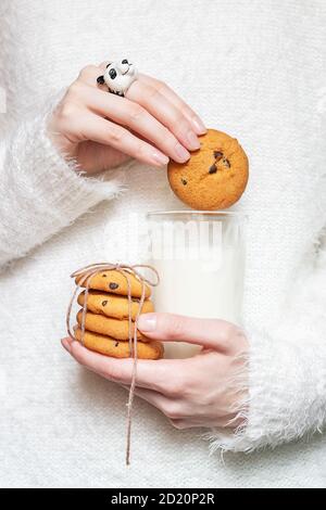 Ein Mädchen in einem weißen flauschigen gemütlichen Winter Pullover hält Hausgemachte Weihnachtskekse und ein Glas Milch in ihr Hände Stockfoto