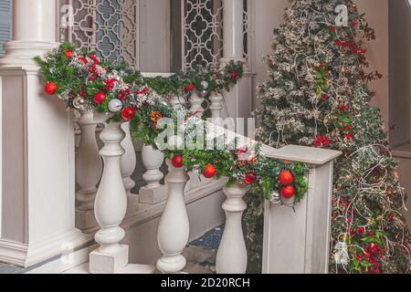 Weihnachten Veranda Dekoration Idee. Hauseingang für Ferien dekoriert. Rote und grüne Kranzgirlande aus Tannenzweigen und Lichtern auf Geländer. Heiligabend zu Hause. Stockfoto