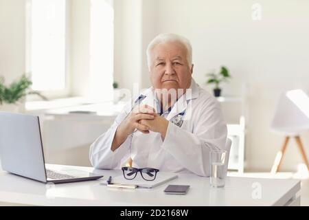 Seriöser Oberarzt sitzt am Schreibtisch mit Laptop im Krankenhaus Büro mit Blick auf die Kamera Stockfoto