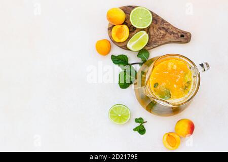Aprikosencocktail oder Eistee mit frischer Minze, Limette und Aprikosen. Erfrischendes kaltes Getränk im Sommer. Heller Betonhintergrund. Draufsicht. Stockfoto