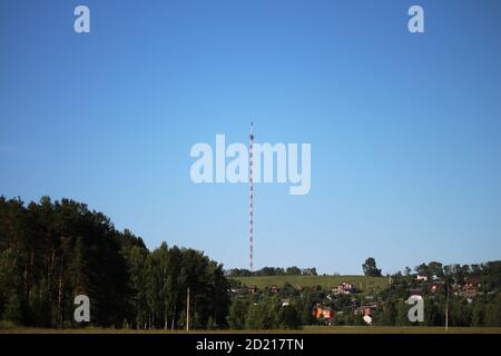 Radio-tv-Turm mit Kabelsalat gegen klaren tiefblauen Himmel, Nahaufnahme. Rot und weiß Gitter Design Stahlstruktur. Stockfoto