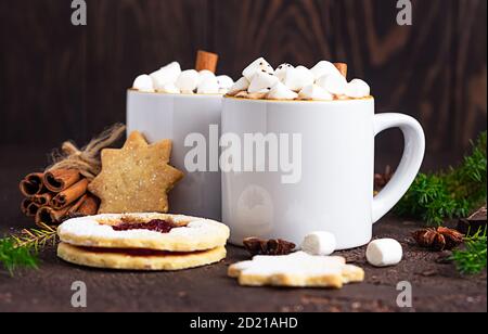 Zwei Tassen heiße Schokolade oder Kakao mit Marshmallow und Zimtstange, Bitterschokolade, Wintergewürzen und Marmelade füllenden Keksen. Festliche Weihnachten oder Stockfoto