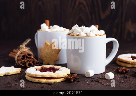 Zwei weiße Keramikbecher mit heißem Kakao oder Schokolade mit Marshmallow und Anis, Zimt und Bitterschokolade auf dunkelbraunem Steingrund. Stockfoto