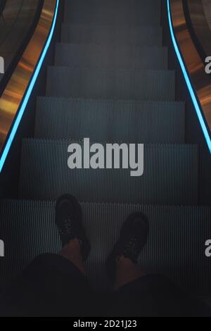 Beine eines Mannes in schwarzen Sneakers auf einer Rolltreppe Stockfoto