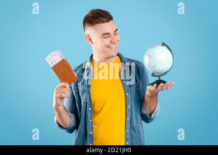 Schöner Mann mit Dokumenten und Globus bereit für Reise um Welt auf blauem Studiohintergrund Stockfoto