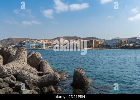 Künstlich geschnittene Felsen stehen im Vordergrund des Blickes auf eine Stadt mit imposanten Gebäuden am Meer und Hügeln im Hintergrund unter bewölktem Himmel. Stockfoto