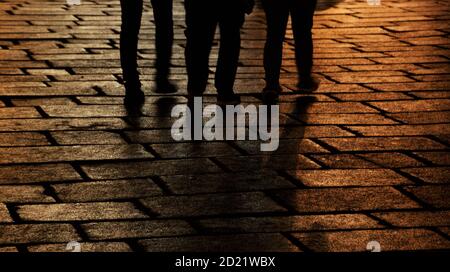 Dunkle Silhouetten von drei Personen, die abends auf der Straße spazieren. Schatten und Lichtreflexion. Städtisches Nachtleben Moderne Ballettszene. Abstraktes Mysterium Stockfoto