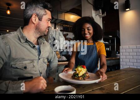 Die Kellnerin in African America serviert gutaussehende Männergerichte im funky Restaurant. Stockfoto