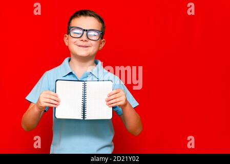 Cuccessful ernst kaukasischen Jungen in einem hellblauen T-Shirt und Brille hält, zeigt mit Finger auf leere Notebook-Banner. Boy zeigt Leerzeichen. Helle r Stockfoto