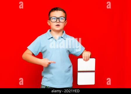 Cuccessful ernst kaukasischen Jungen in einem hellblauen T-Shirt und Brille hält, zeigt mit Finger auf leere Notebook-Banner. Boy zeigt Leerzeichen. Helle r Stockfoto