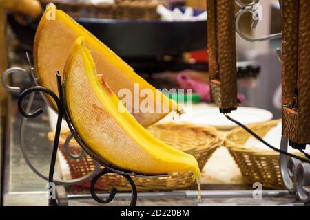 Raclette (traditionelles geschmolzenes Käsegericht) Stand auf dem Weihnachtsmarkt in Paris. Tropfender gelber Käse. Abstrakt traditionelle Lebensmittel Hintergrund. Foodie tou Stockfoto