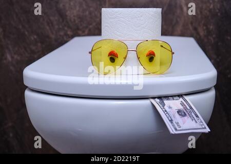 Toilettenschüssel mit Augen in Form von Toilettenpapier Essen Geld in US-Dollar, lustiges Konzept Stockfoto