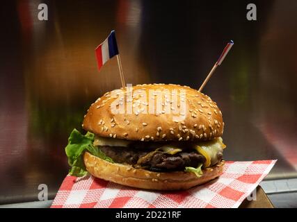 Frankreich Street Food. Frischer, leckerer Burger mit Käse und französischen Flaggen am Food Track Counter. Verschwommene Reflexion. Fast Food Hintergrund. Stockfoto