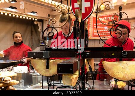 PARIS, FRANKREICH - 6. JANUAR 2019: Junge Frau bereitet am traditionellen Savoie-Imbissstand auf dem Weihnachtsmarkt in TU geschmolzenes Raclette-Käse-Sandwich zu Stockfoto