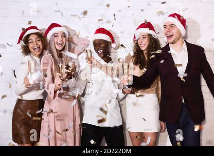 Menschen In Santa Hats Klirrende Gläser Unter Fallenden Konfetti Indoor Stockfoto