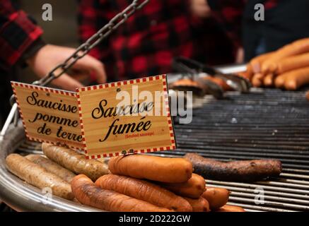 Verschiedene Grillwürste auf der Straße Weihnachtsmarkt Stand in Paris, Frankreich. Die Anbieter sind im Hintergrund. Selektiver Fokus. Stockfoto