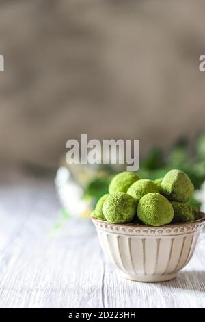 Hausgemachte Trüffelbonbons mit grünem Matcha-Tee in einer Keramikschale auf hellem Holzhintergrund. Rohe Energiekugeln. Stockfoto