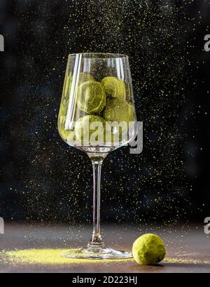 Hausgemachte Trüffelbonbons mit grünem Matcha-Tee in einem Glaskelch auf dunklem Grund. Rohe Energiekugeln. Stockfoto