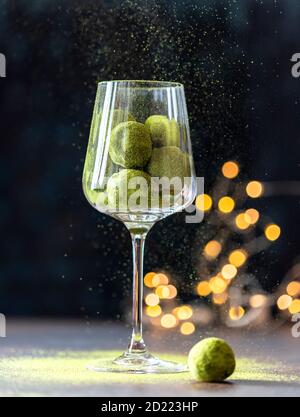 Hausgemachte Trüffelbonbons mit grünem Matcha-Tee in einem Glaskelch auf dunklem Grund. Rohe Energiekugeln. Stockfoto