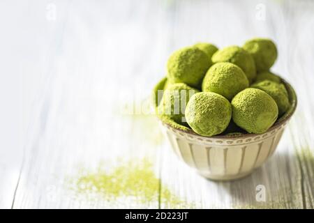 Hausgemachte Trüffelbonbons mit grünem Matcha-Tee in einer Keramikschale auf hellem Holzhintergrund. Rohe Energiekugeln. Stockfoto