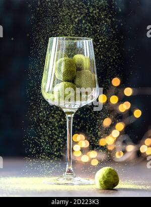 Hausgemachte Trüffelbonbons mit grünem Matcha-Tee in einem Glaskelch auf dunklem Grund. Rohe Energiekugeln. Stockfoto