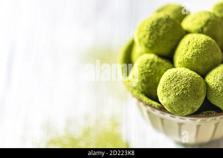 Hausgemachte Trüffelbonbons mit grünem Matcha-Tee in einer Keramikschale auf hellem Holzhintergrund. Rohe Energiekugeln. Stockfoto