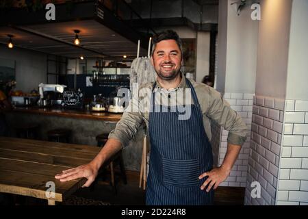 Gut aussehende männliche Coffee Shop Besitzer stehen fröhlich in seinem Coffee Shop. Stockfoto
