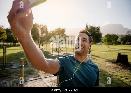 Junger männlicher Athlet, der sich mit dem Smartphone-Hören fotografiert Zu Musik mit Ohrhörern im Park Stockfoto